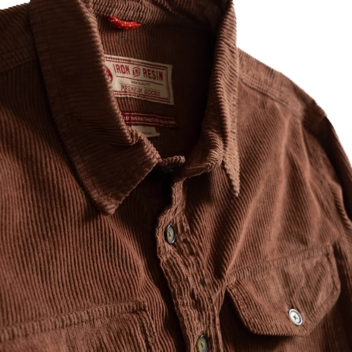Close-up of a brown corduroy button-up shirt collar and chest area, showing the Iron Resin brand label inside the neck and metal buttons on a white background.