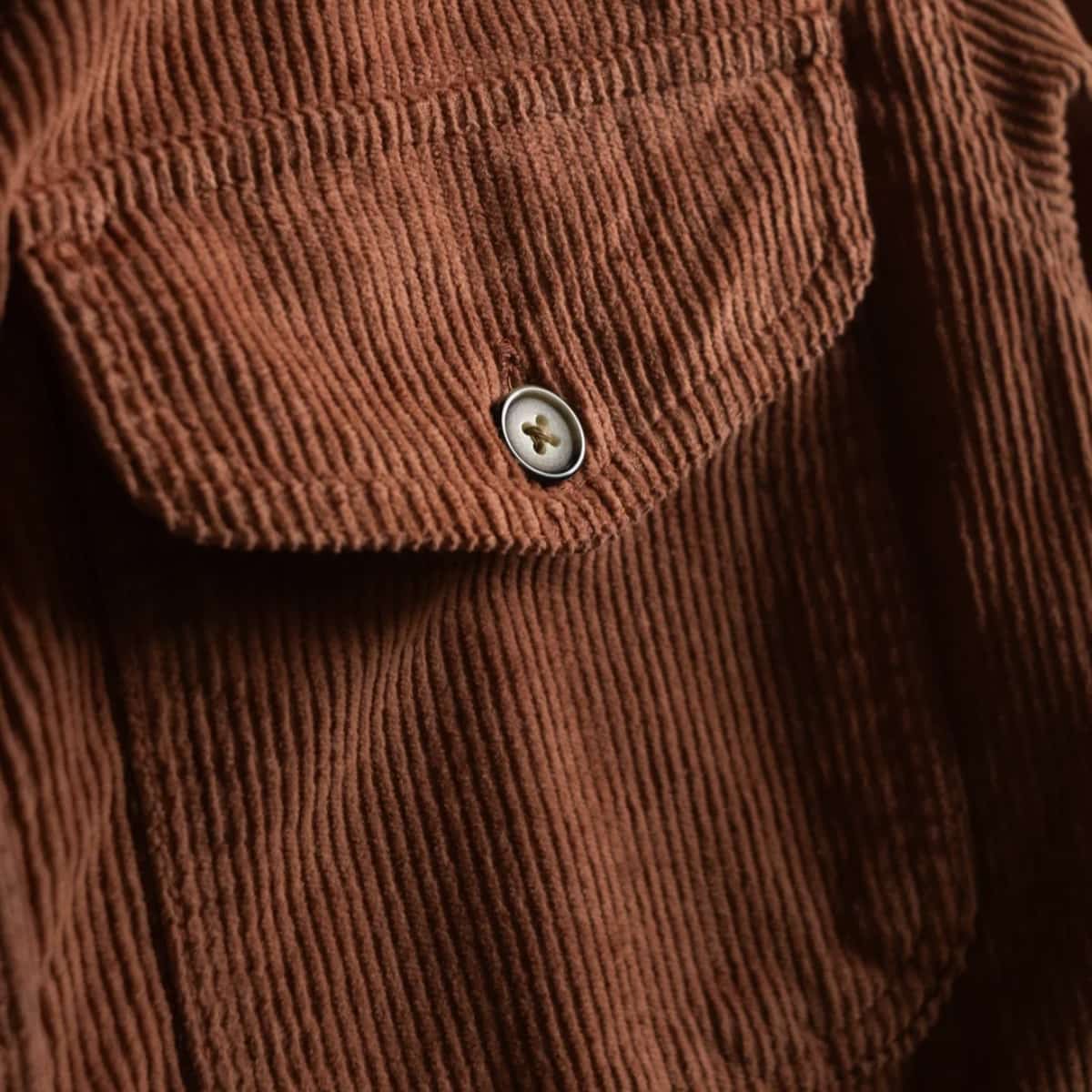 Close-up of a brown corduroy jacket showing a chest pocket with a button closure.
