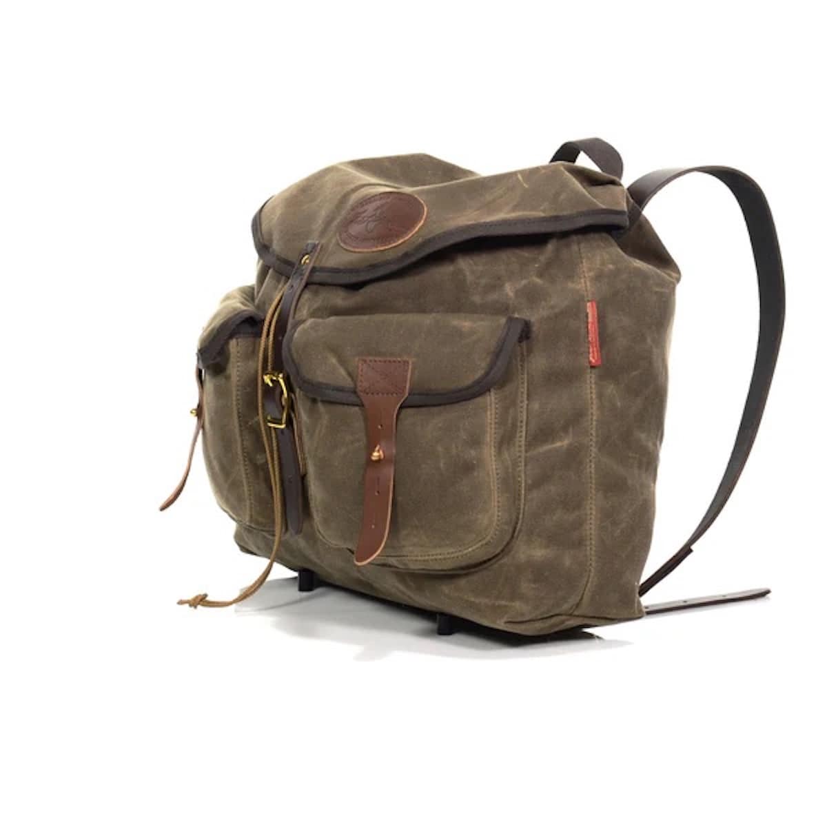 A rugged waxed canvas Frost River bag in olive brown with dark brown leather trim, front utility pockets, brass-tone hardware, and a detachable shoulder strap, photographed on a clean white background.