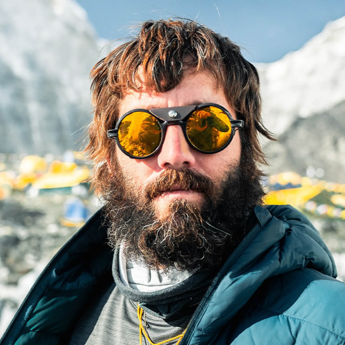 Man with sunglasses and beard in front of a mountainous landscape