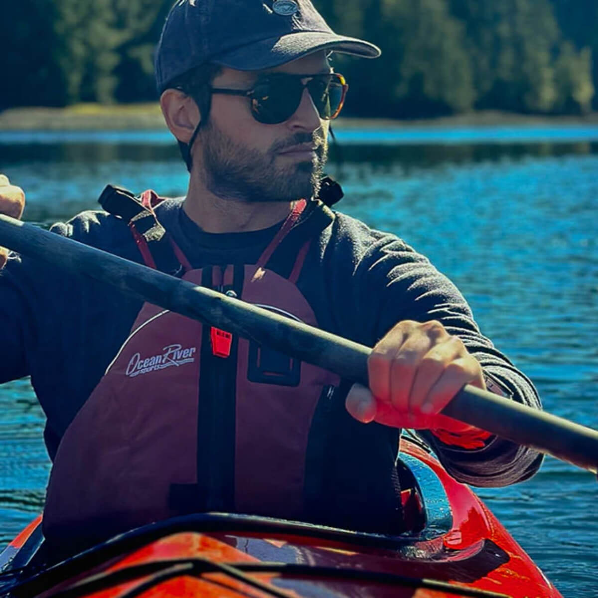 Man paddling a kayak on a body of water with trees in the background