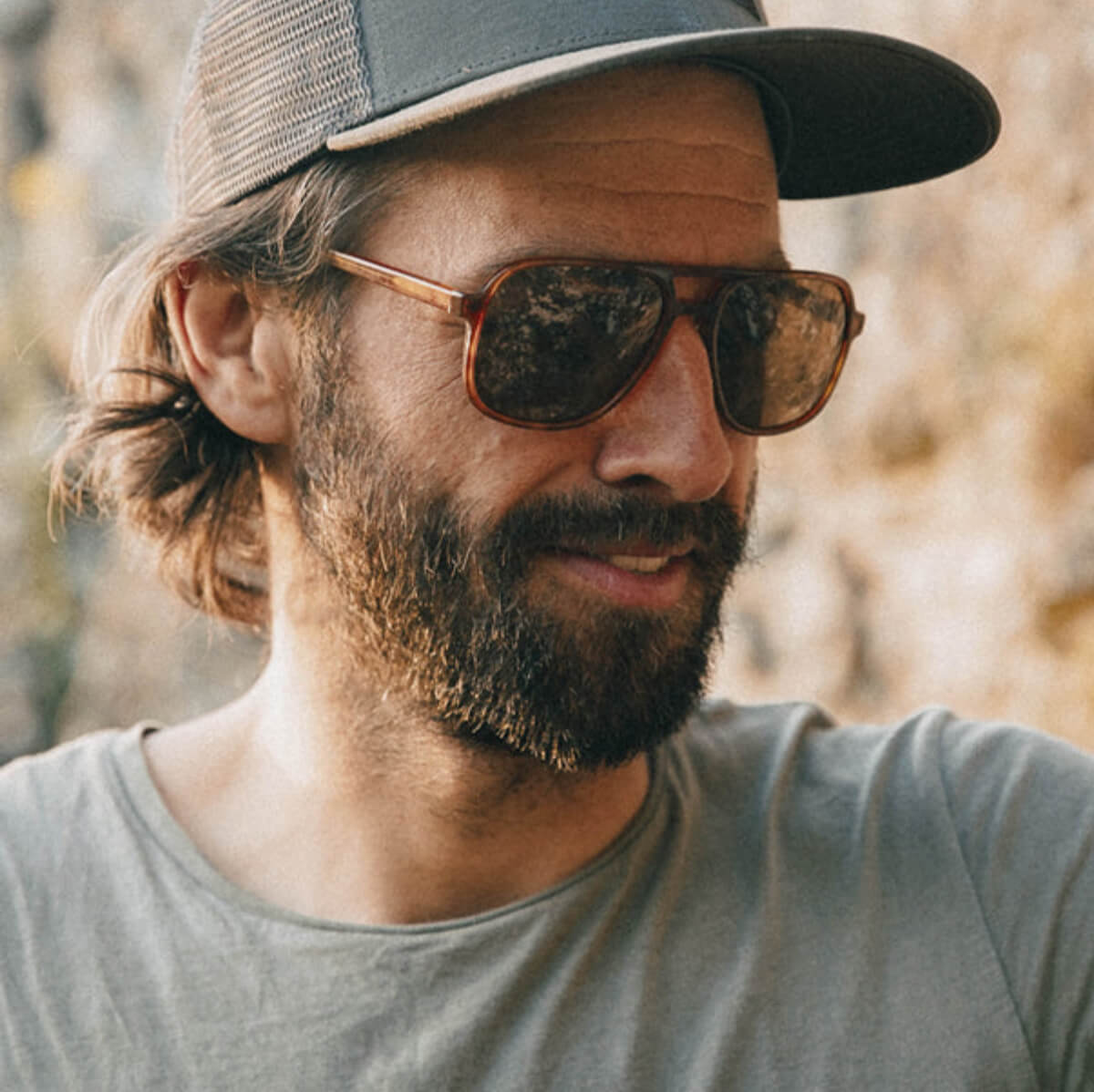 Man wearing sunglasses and a cap with a blurred natural background
