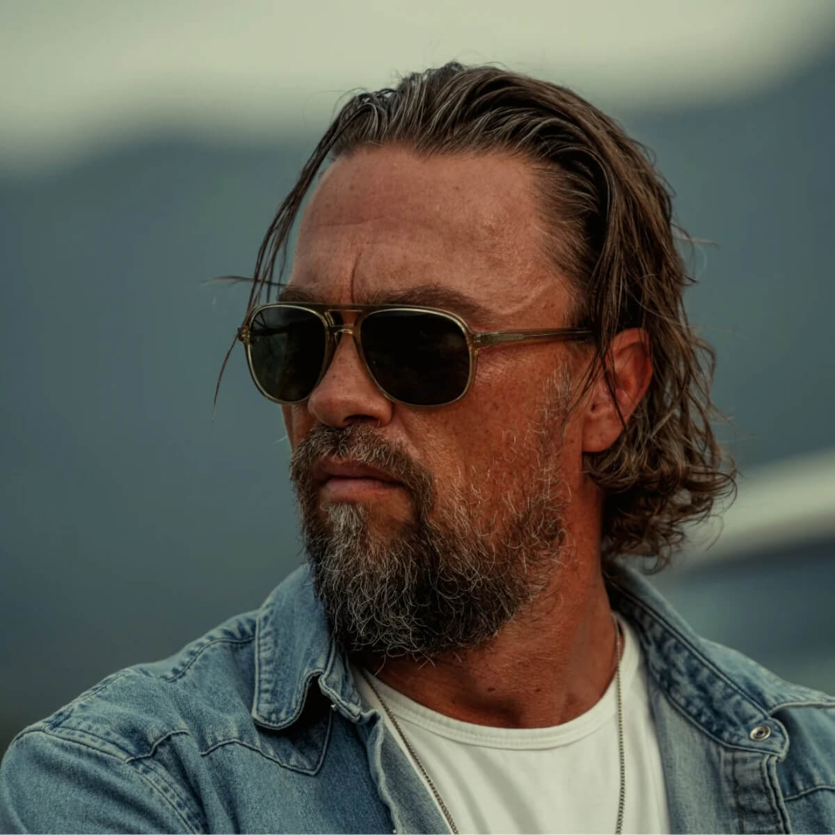 Man wearing sunglasses and a denim jacket with a mountainous background