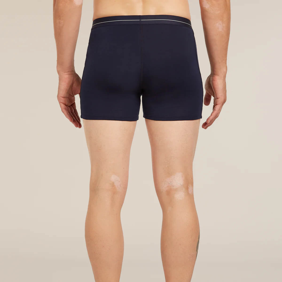 Person wearing navy blue boxer briefs on a beige background