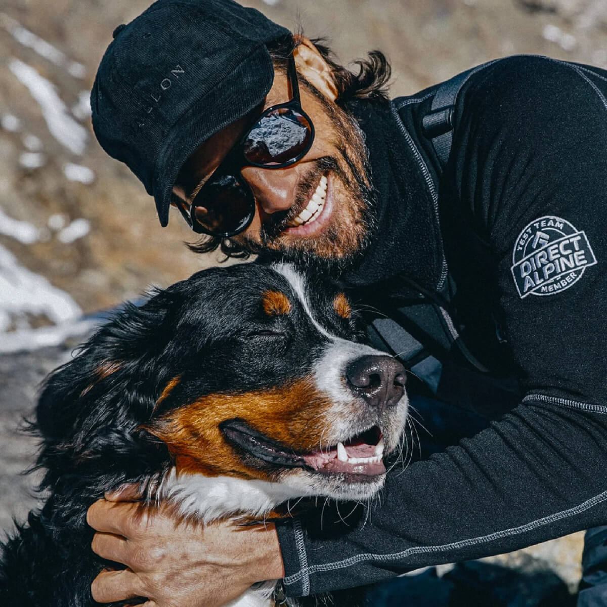 Man hugging a Bernese Mountain Dog outdoors with a snowy background
