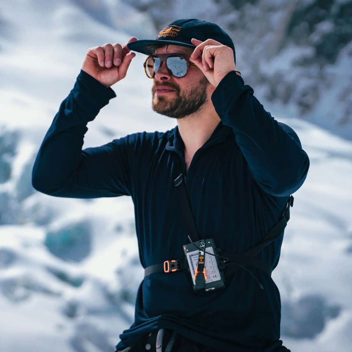 Man adjusting sunglasses with a snowy mountain background