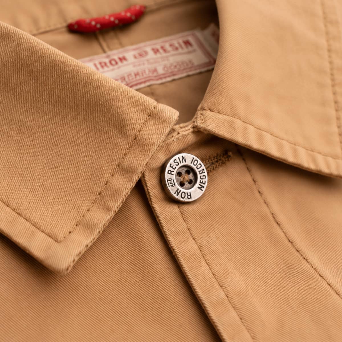 Close-up of a tan jacket with a button and brand label.