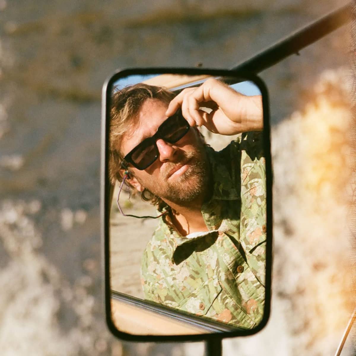 Person wearing sunglasses and a Iron and Resin shirt reflected in a vehicle mirror with a natural background.