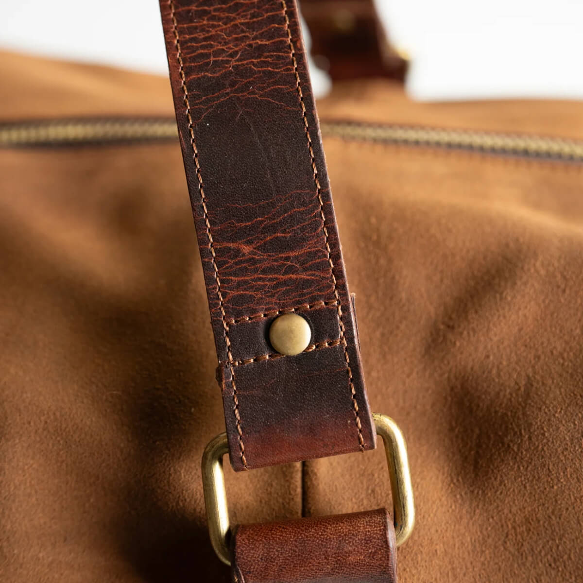 Close-up of a brown leather bag with a strap and button detail.
