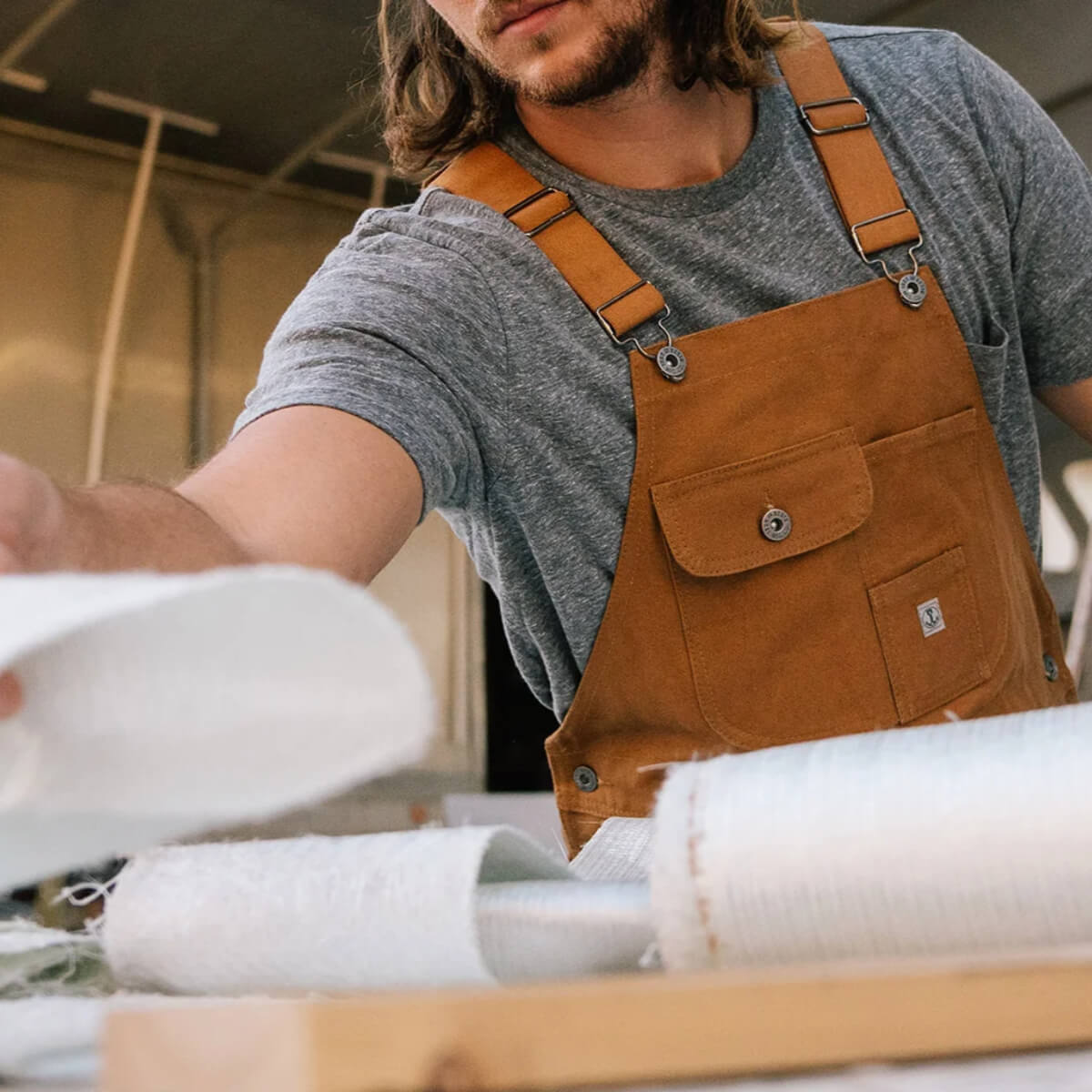 Person wearing brown overalls working with fabric in a workshop setting