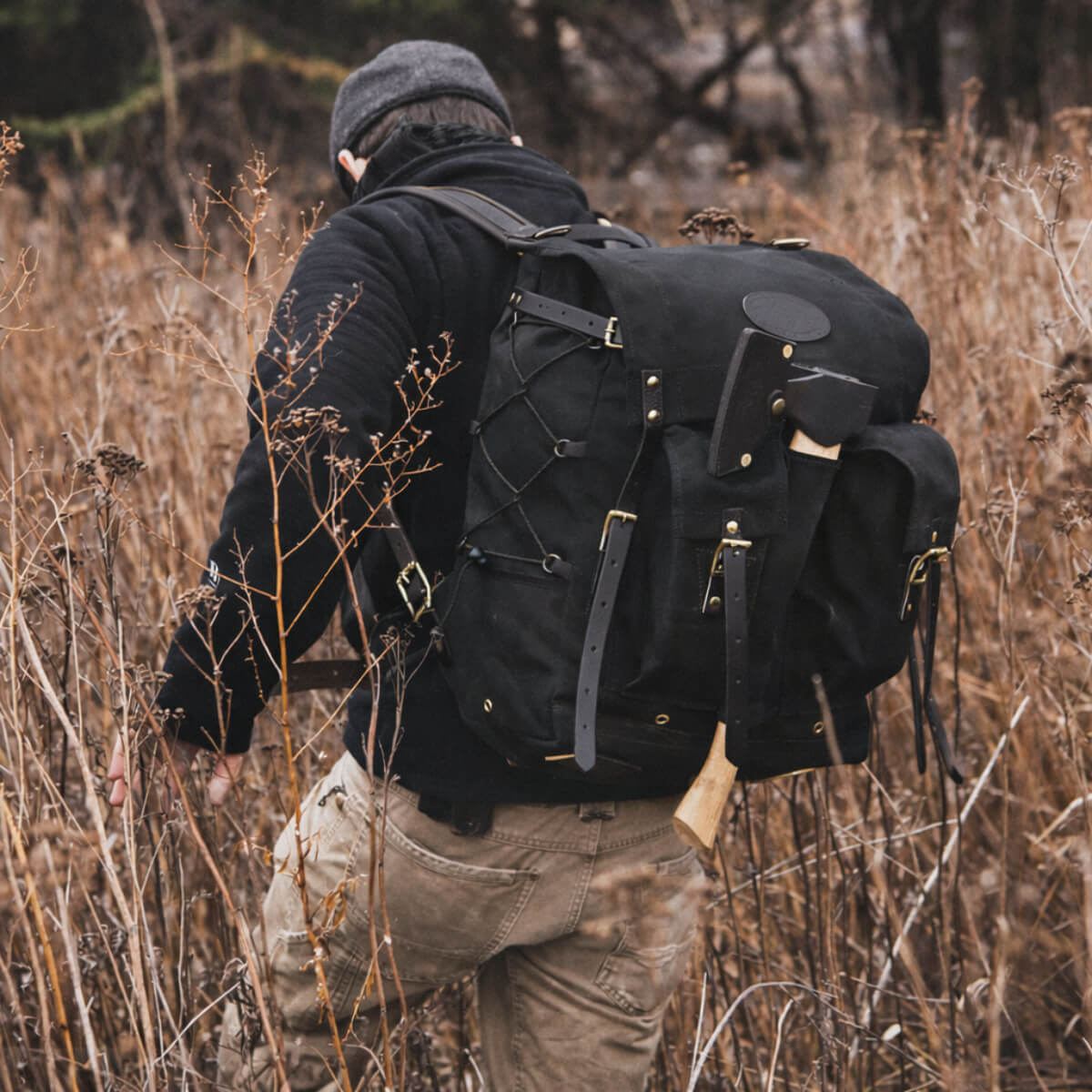Person with a large black backpack walking through a field of dry grass.
