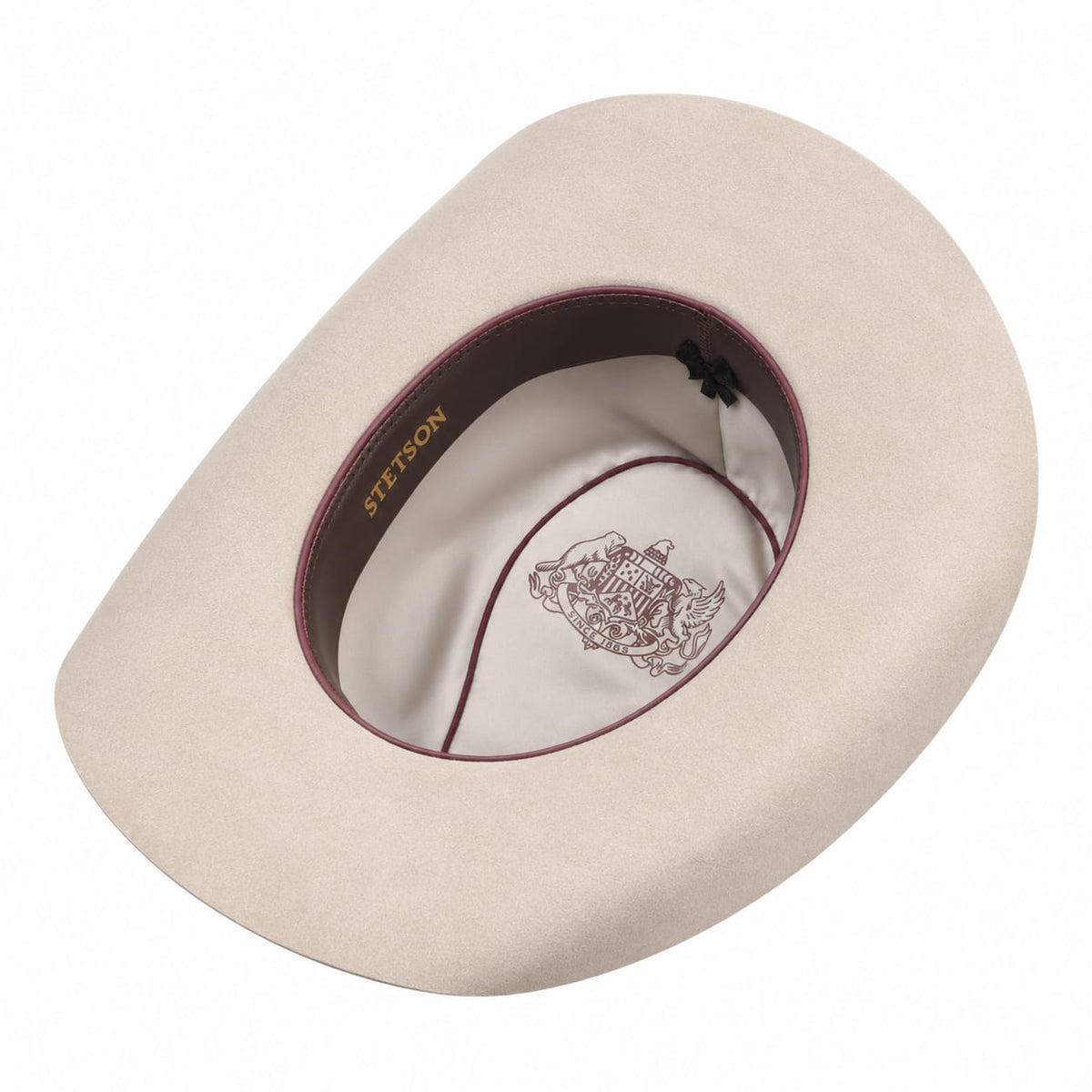 A light beige cowboy hat shown from a top-down angle, featuring a dark burgundy inner band with gold 'STETSON' branding and a white interior crown lining with a crest illustration.