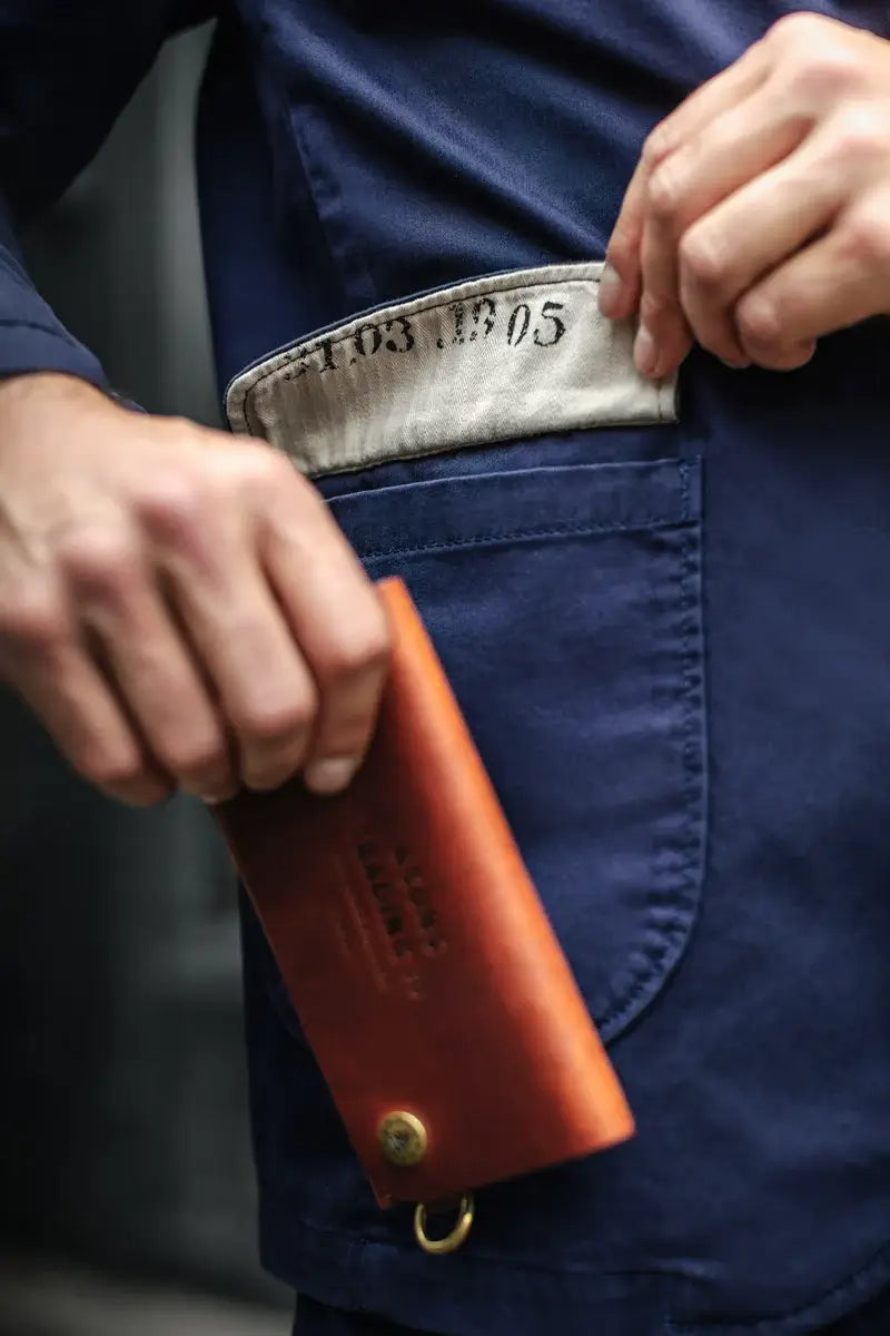 Person wearing a blue uniform with a silver belt buckle, holding an orange leather wallet.