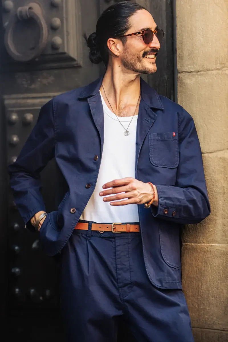 Man wearing a navy jacket and white shirt leaning against a textured wall.