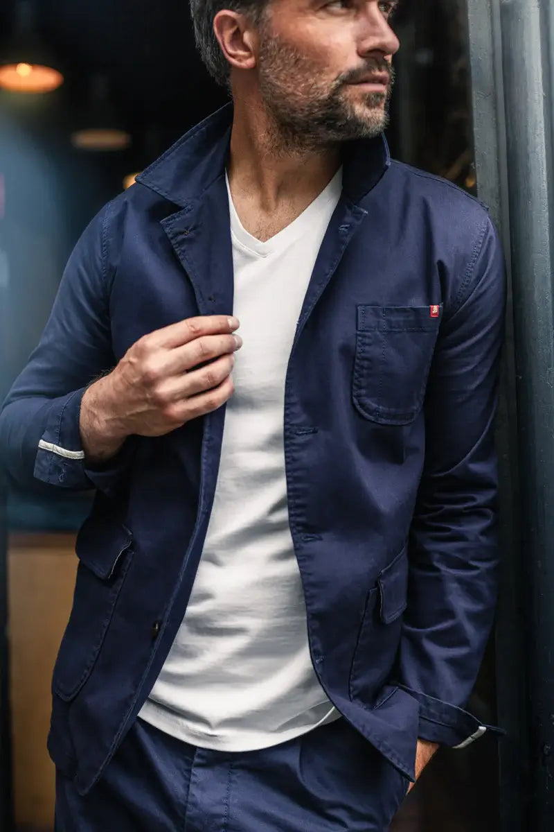 Man wearing a navy jacket over a white shirt, standing indoors.