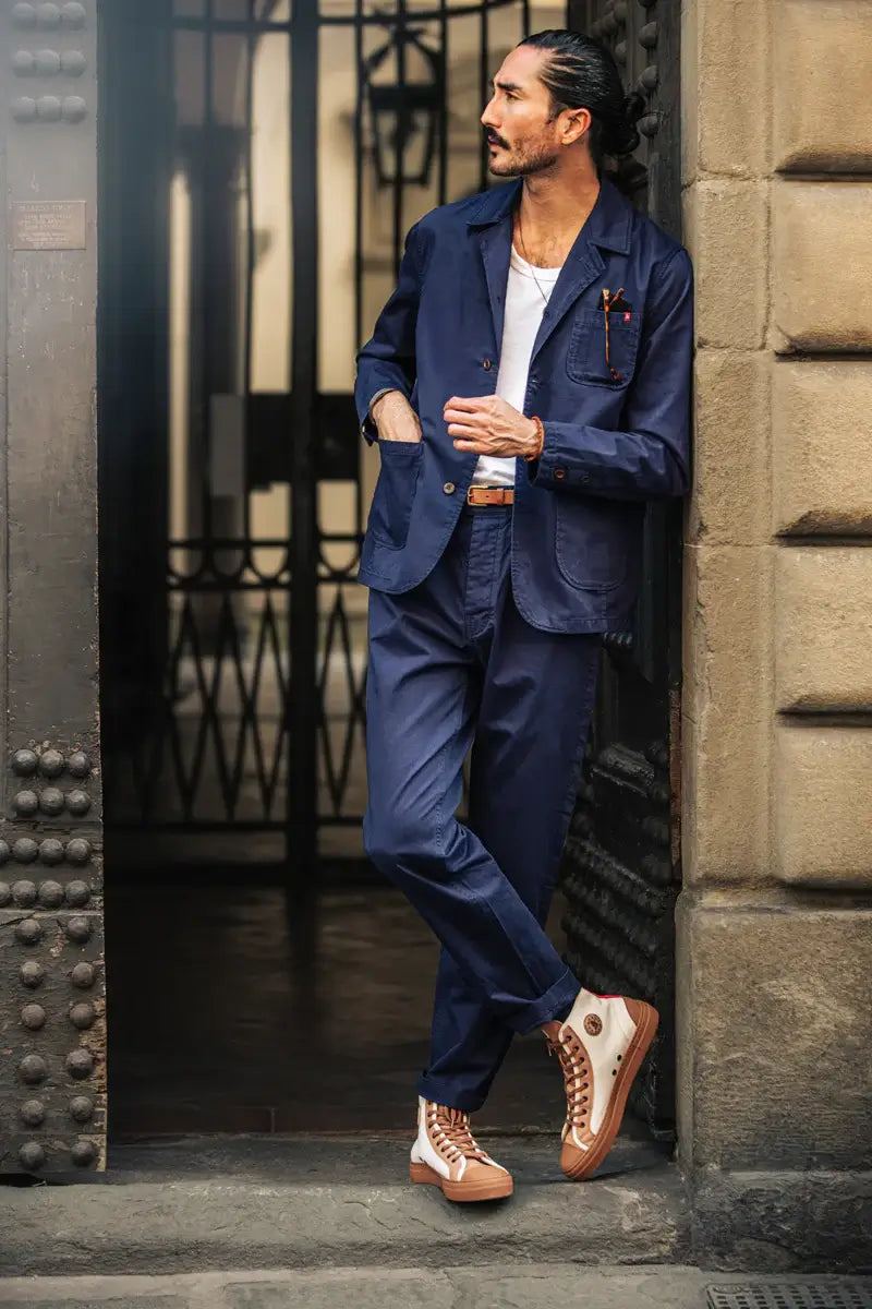 Man in a navy blue suit with brown shoes standing in front of a textured wall.