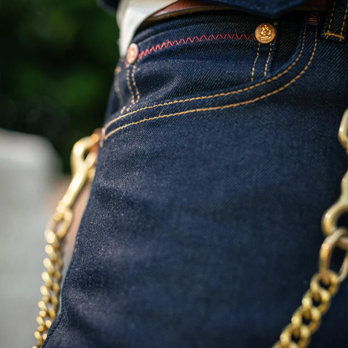 Close-up of dark blue jeans with gold chain detail, blurred background