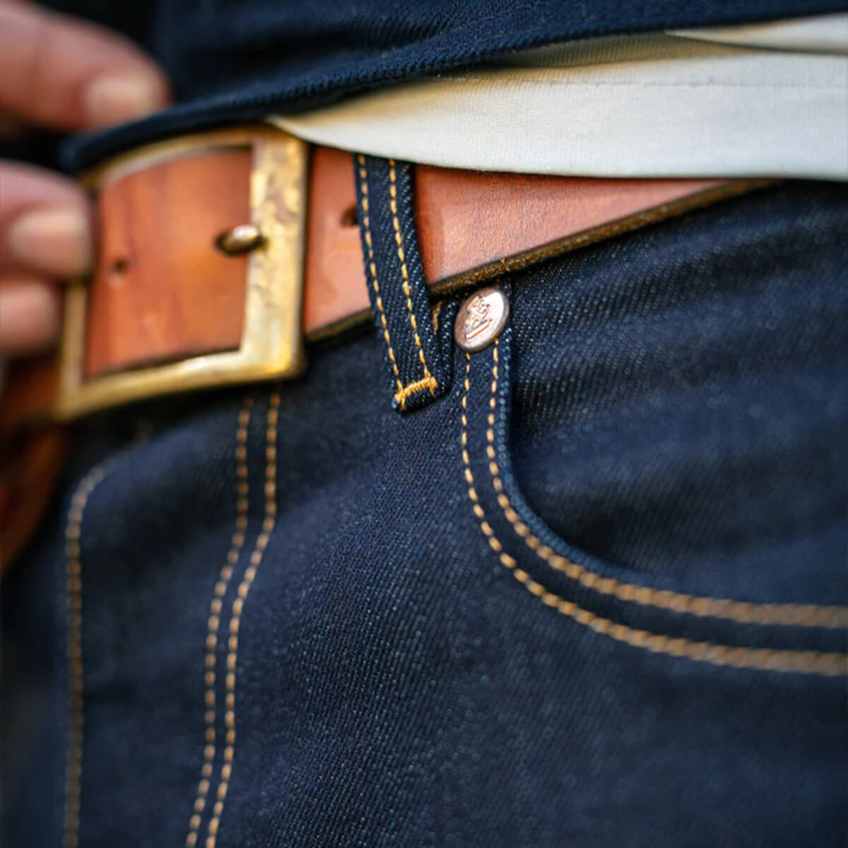 Close-up of blue jeans with a brown belt and gold buckle.