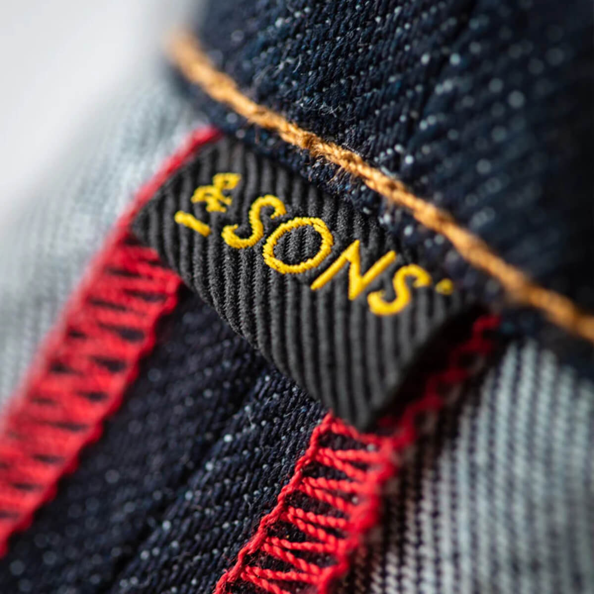 Close-up of a denim label with 'SONS' text on a textured fabric background
