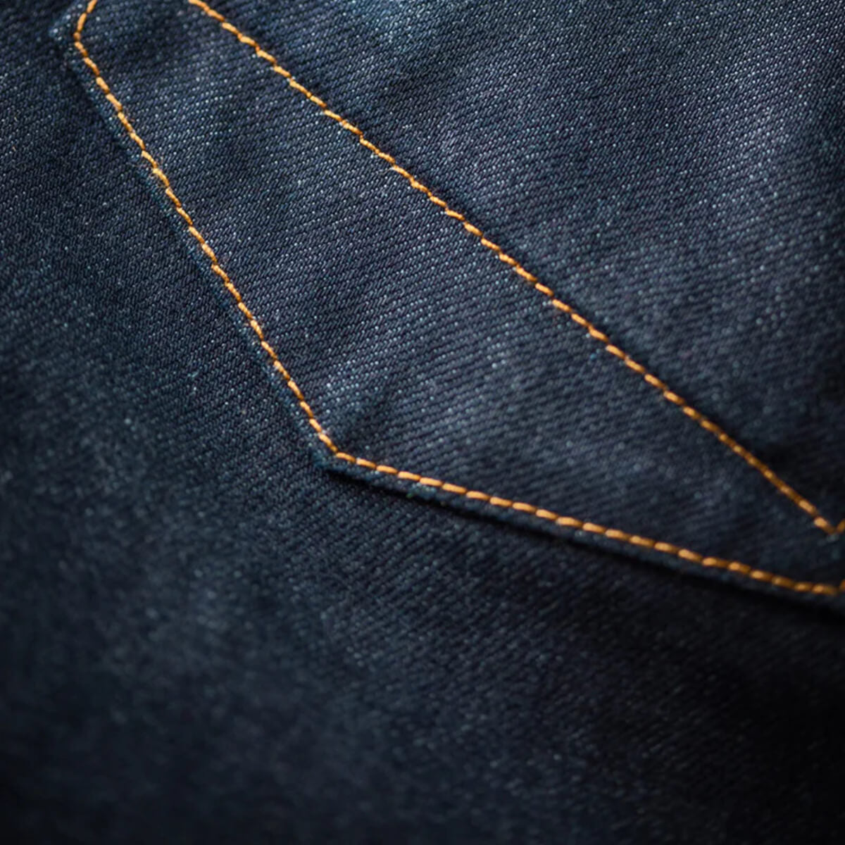 Close-up of dark blue denim fabric with orange stitching