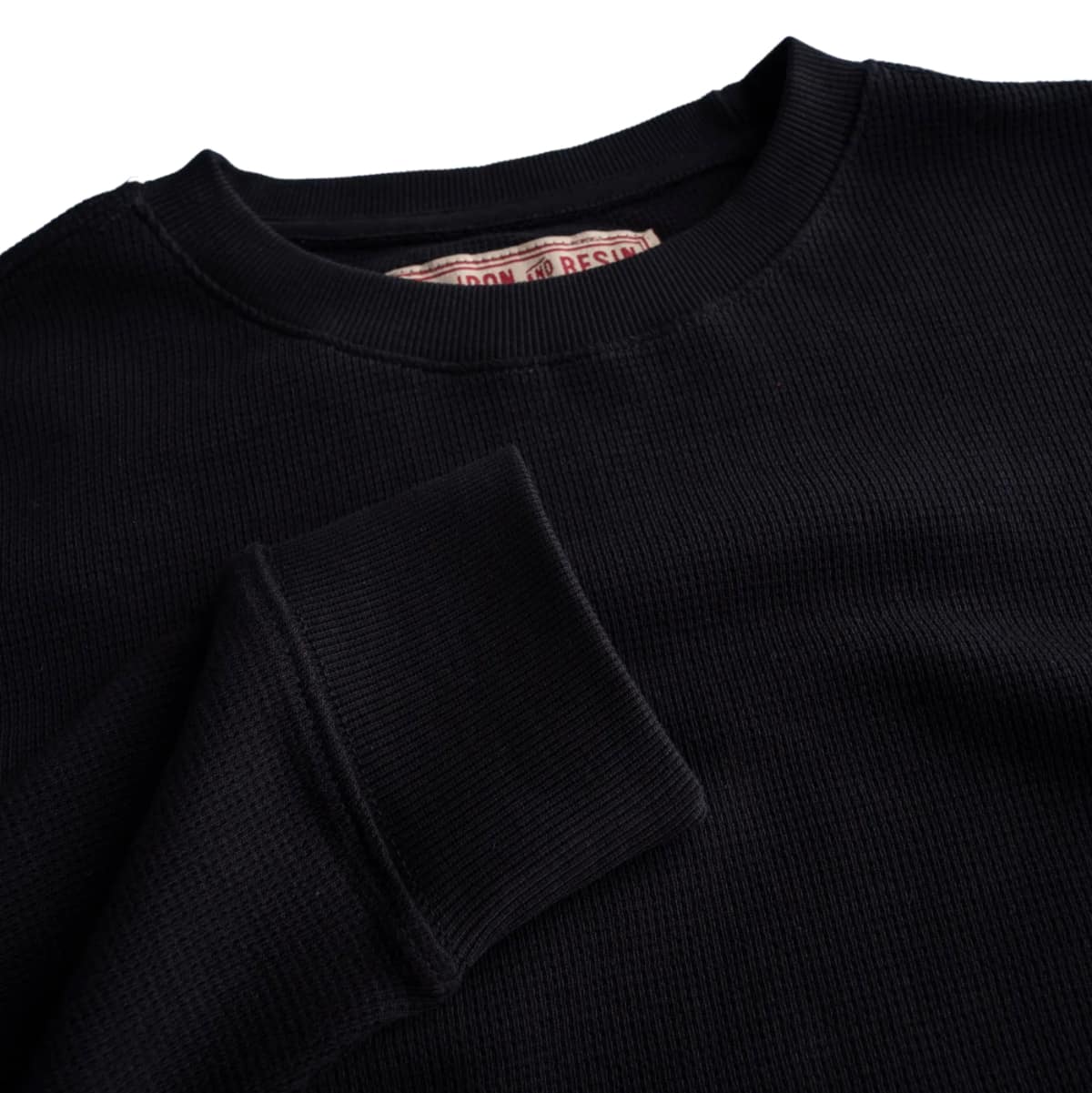 Close-up of a blackIron and Resin Cotton Crewe Neck, showing the collar and a folded sleeve detail against a white background.