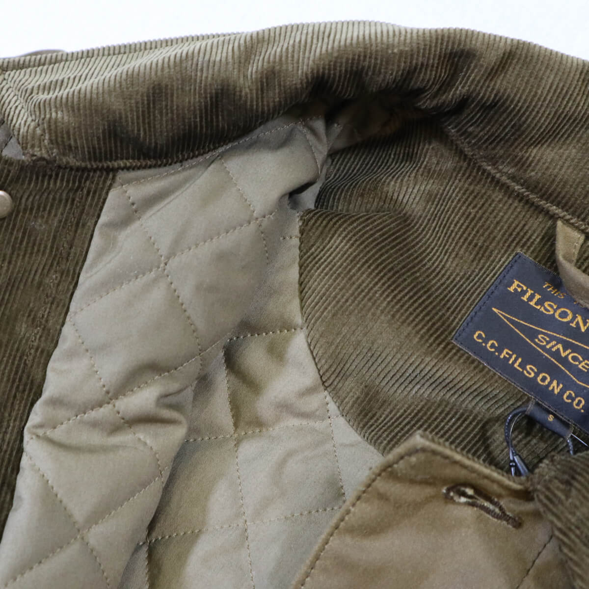 Close-up of a quilted jacket with a Filson label on a white background