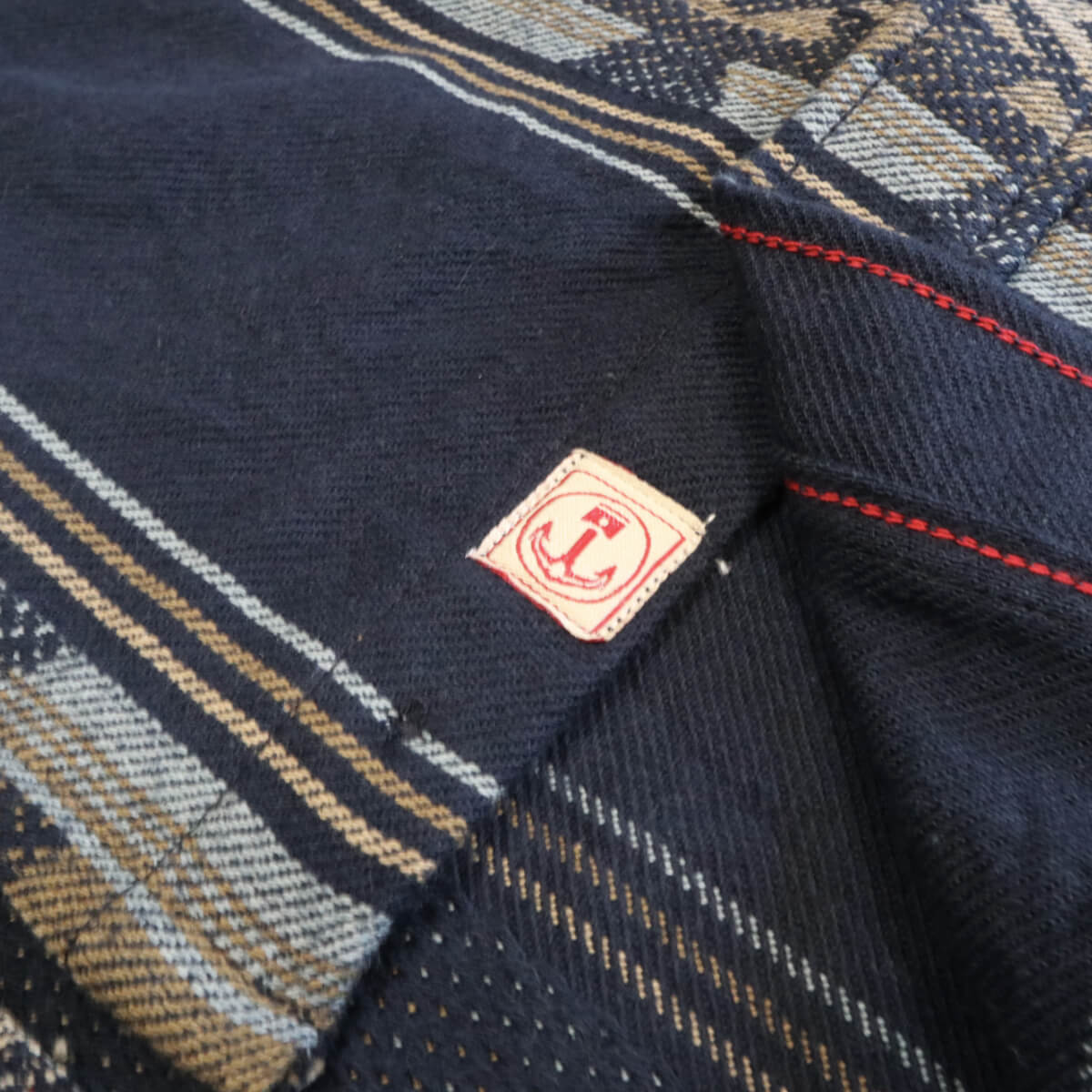 Close-up of a navy fabric with a brand logo, featuring red stitching.