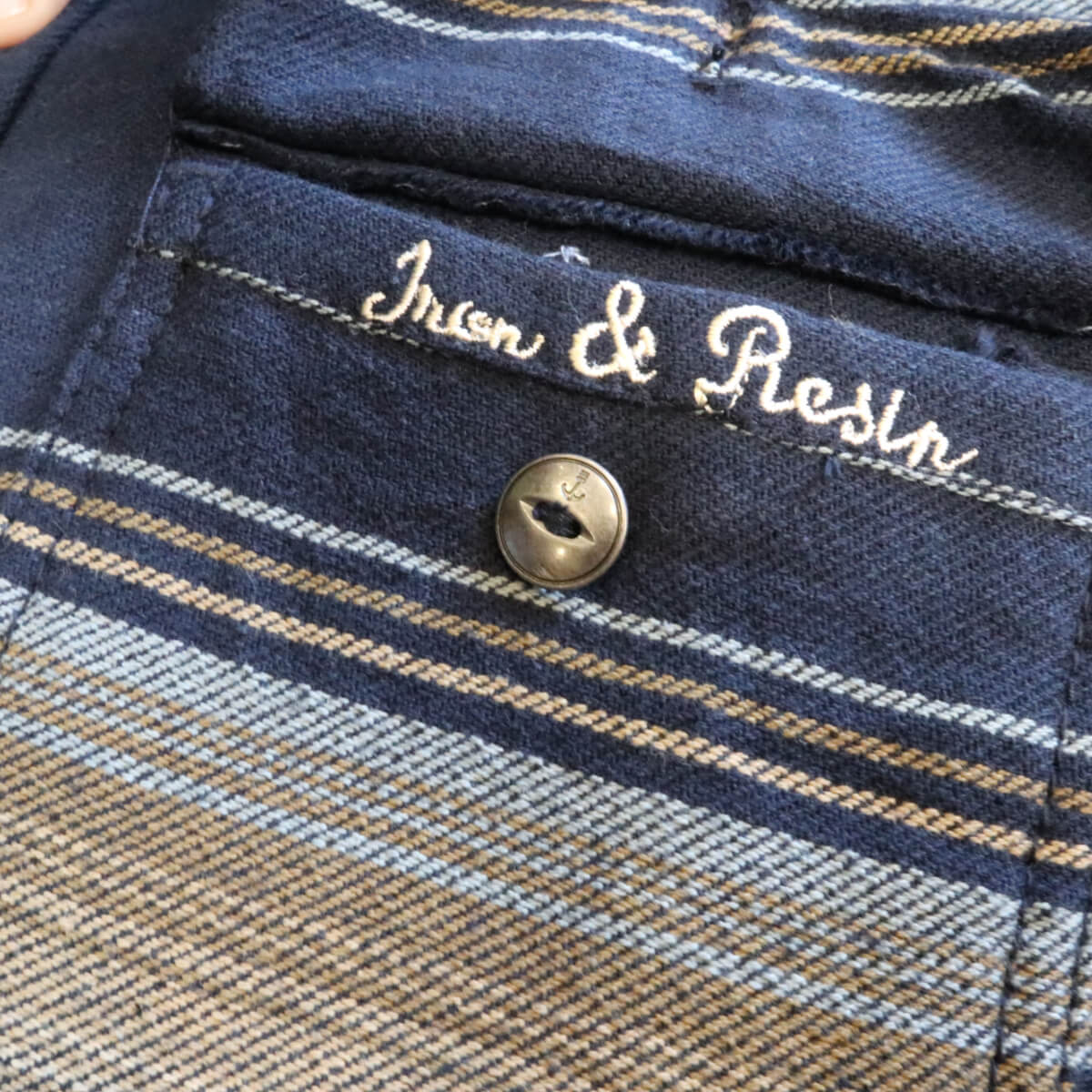 Close-up of a plaid fabric with &#39;Iron &amp; Resin&#39; branding and a button.