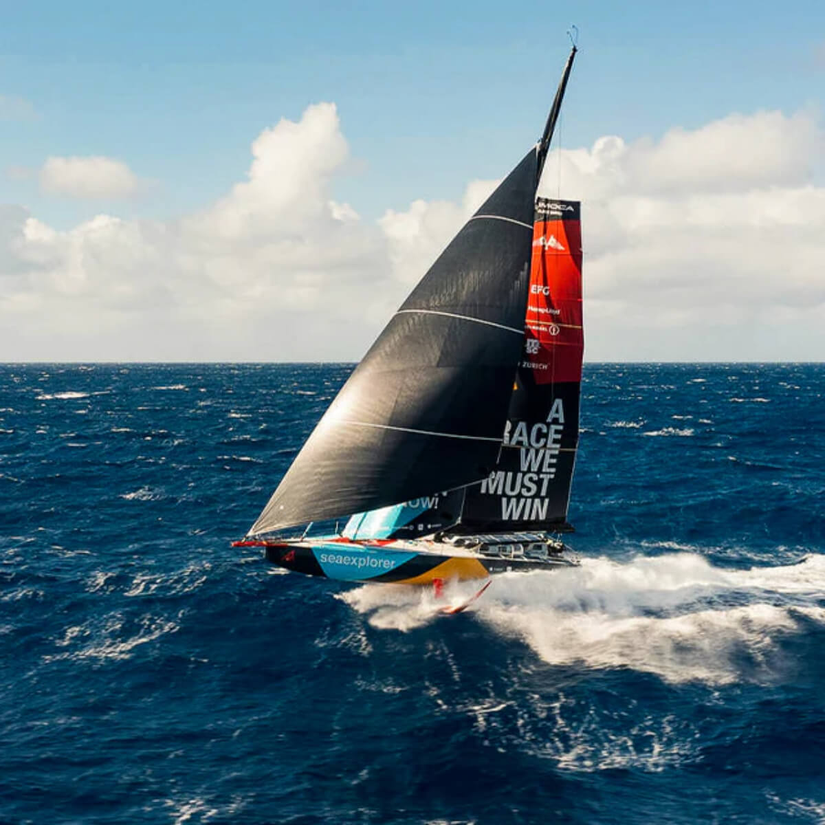 Sailboat with a large sail on the ocean under a blue sky with clouds.