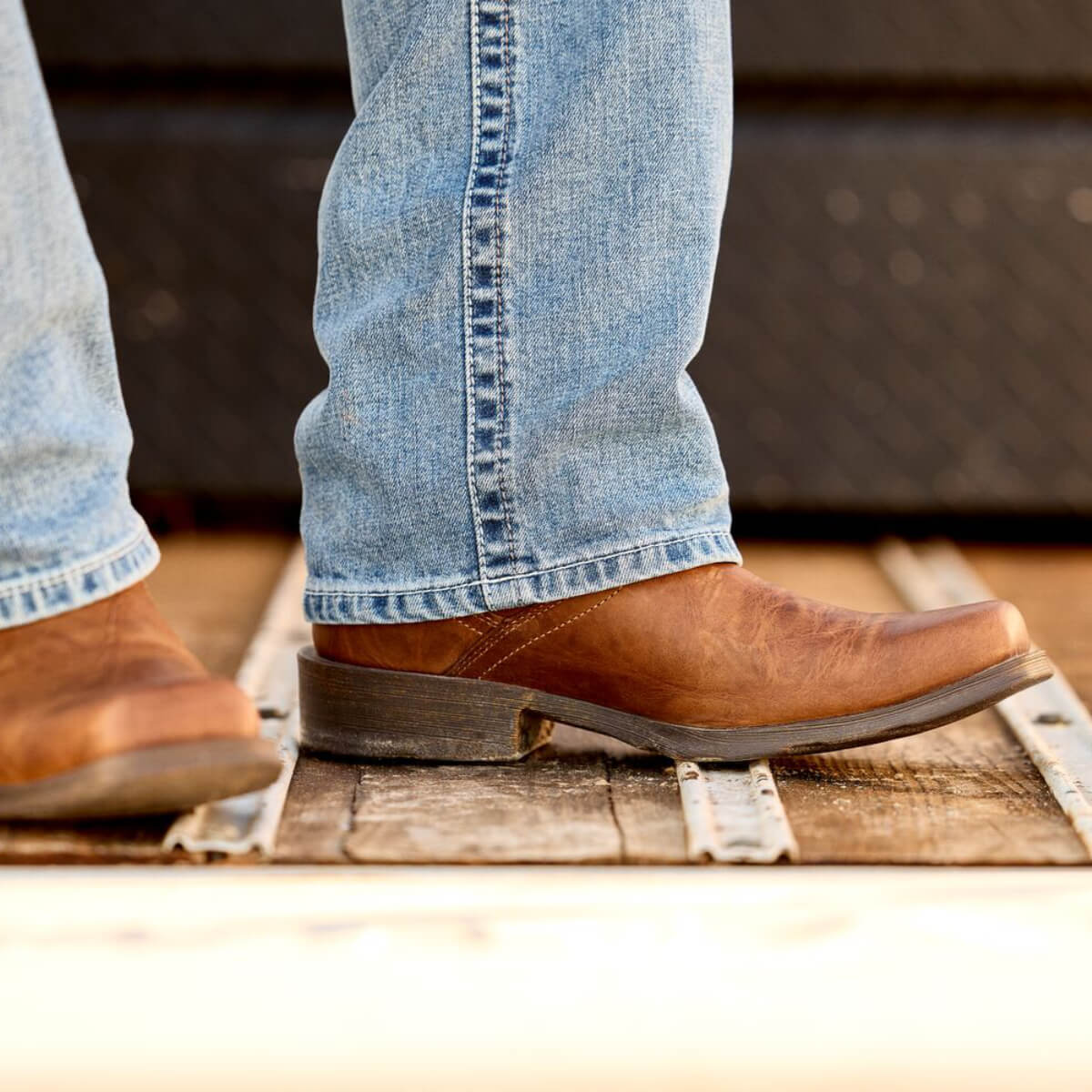 Close-up of brown leather boots and blue jeans on a wooden floor.
