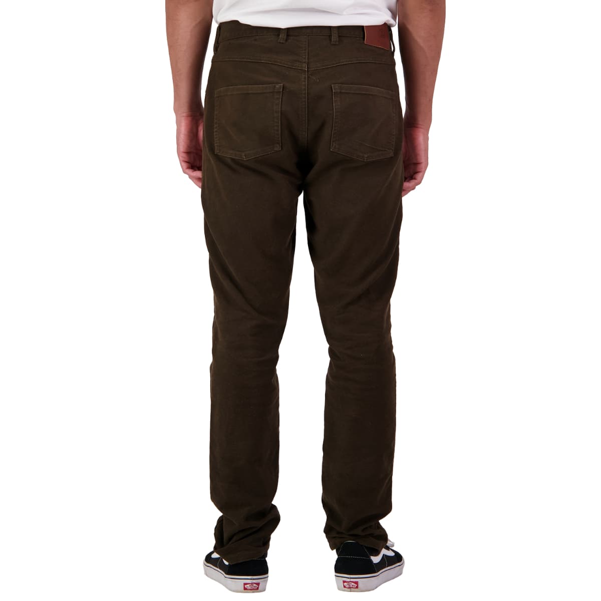 A person shown from the back wearing dark brown slim-fit pants, a white t-shirt, and black sneakers with white soles against a plain white background.