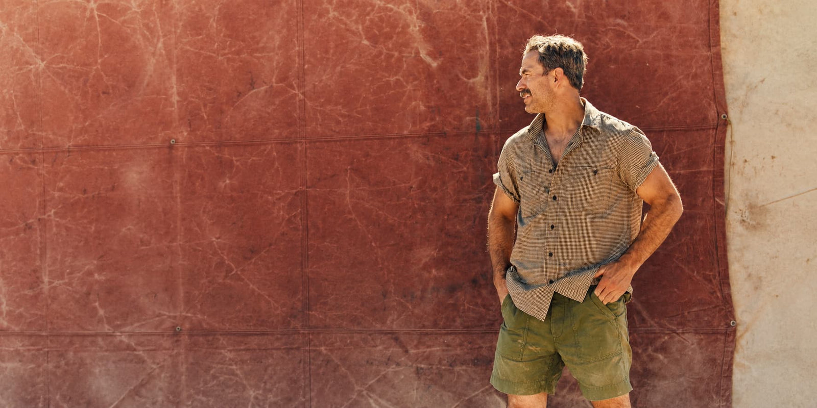 Man wearing Filson shirt and shorts standing against red wall