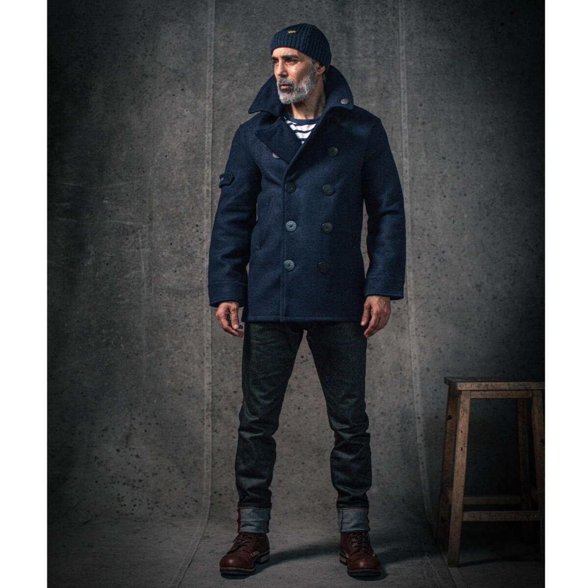 Man wearing a navy blue coat and hat against a gray background