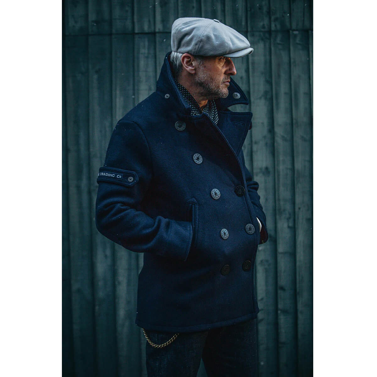 Man wearing a dark blue coat and gray cap against a dark background