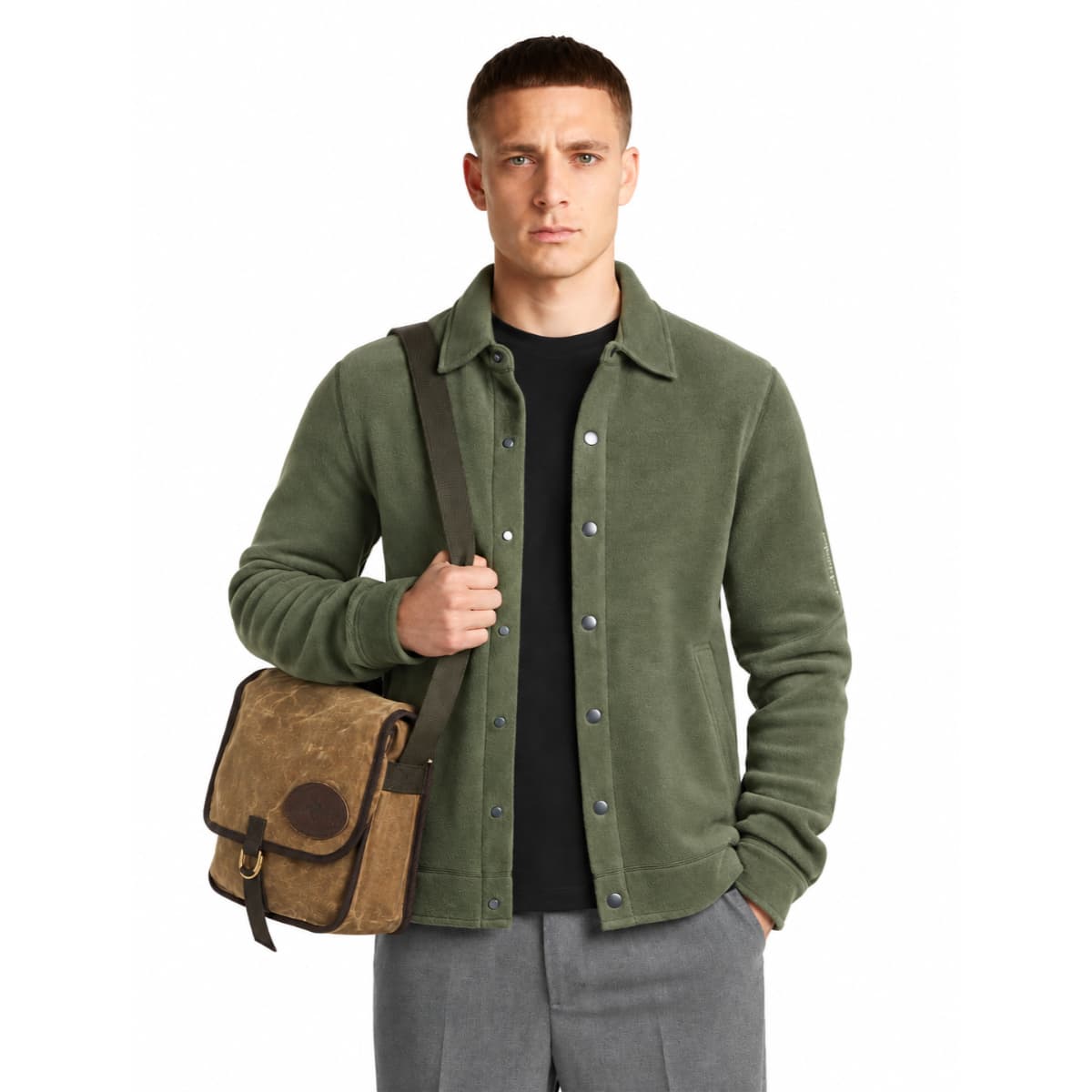 A man wearing an olive green Icebreaker merino wool shacket over a black t-shirt and gray trousers, carrying a brown canvas messenger bag with a dark strap.