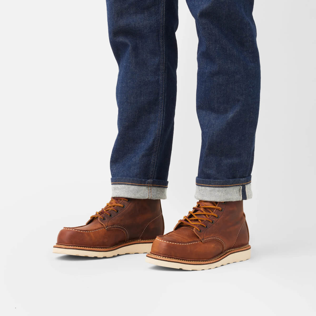 Brown leather boots with rolled-up jeans on a light gray background