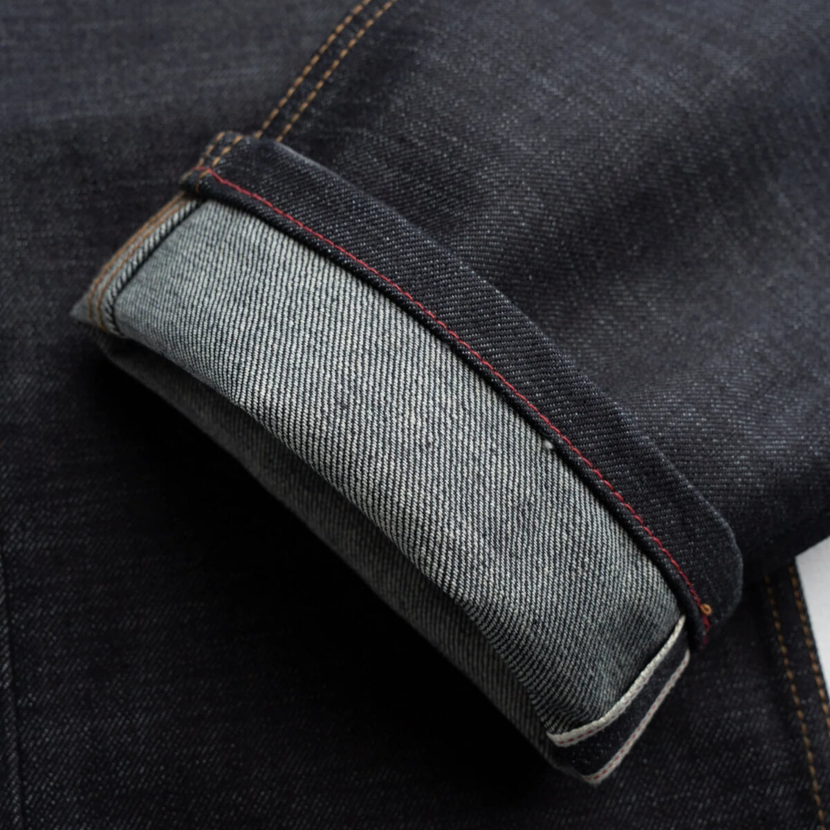 Close-up of dark blue denim fabric with a visible seam and stitching detail.