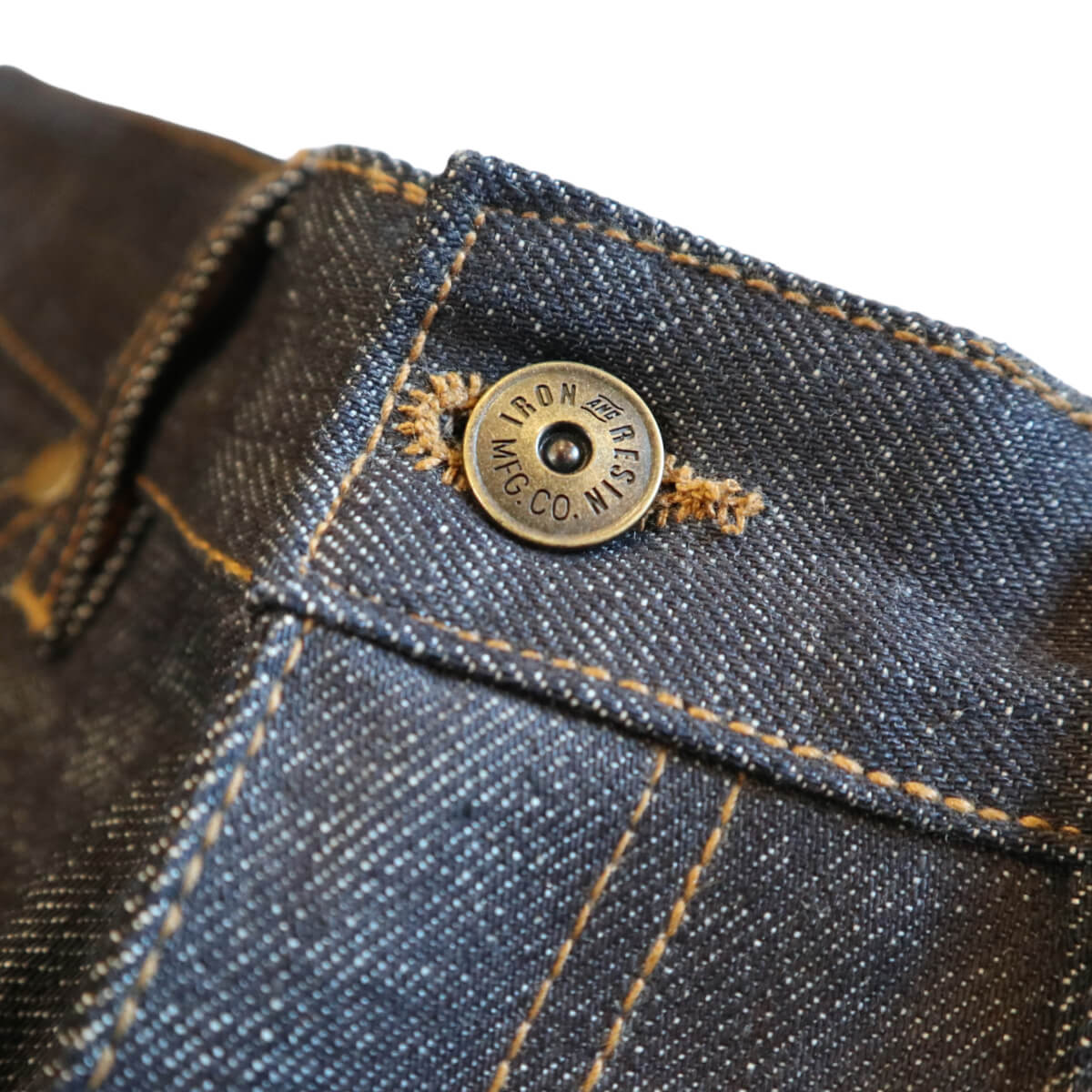 Close-up of a button on a denim jacket with Iron and Resin branding.
