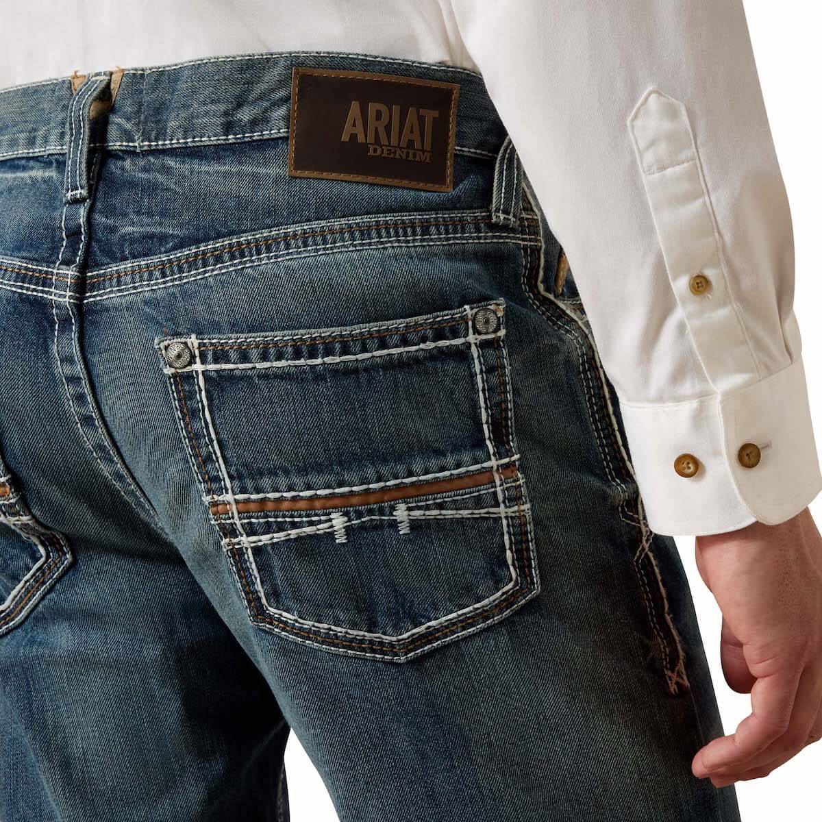 Close-up of blue jeans with Ariat logo and a white shirt.