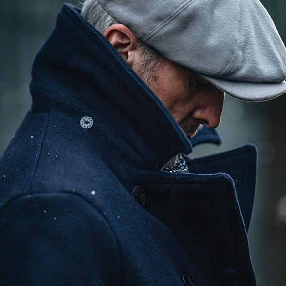 Man wearing a dark coat and gray cap in a snowy setting