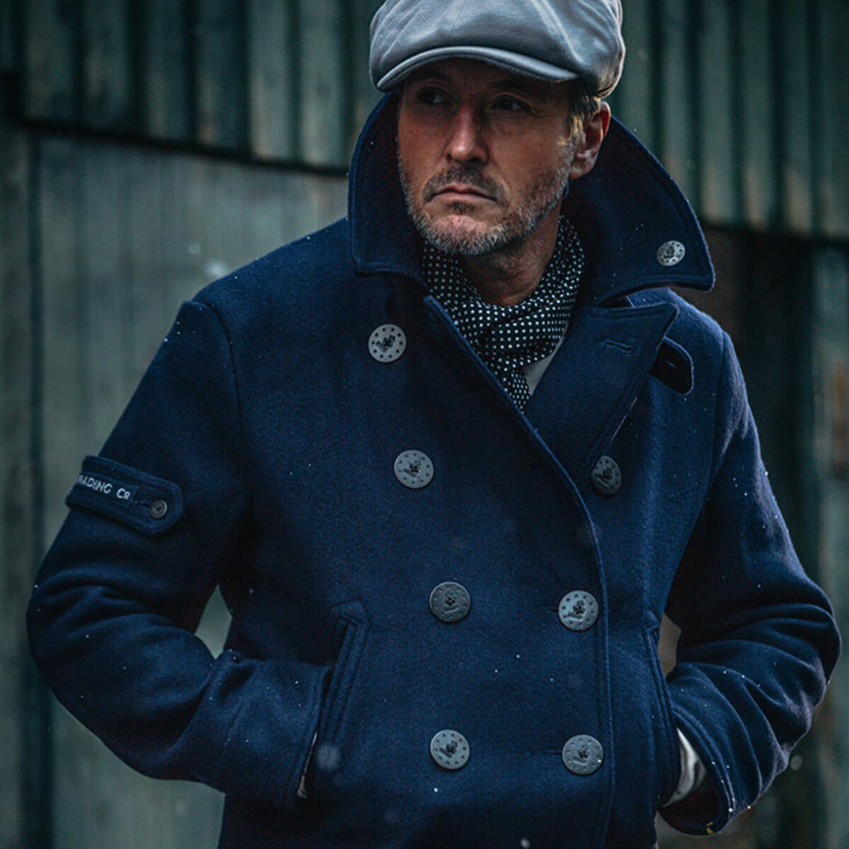 Man wearing a blue coat and cap against a blurred background