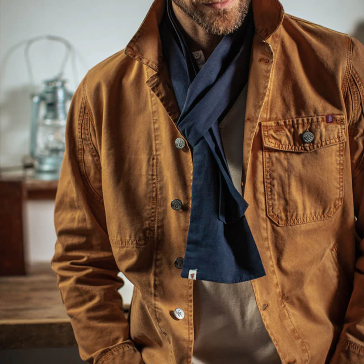 Man wearing a brown jacket with a blue shirt underneath, standing indoors.