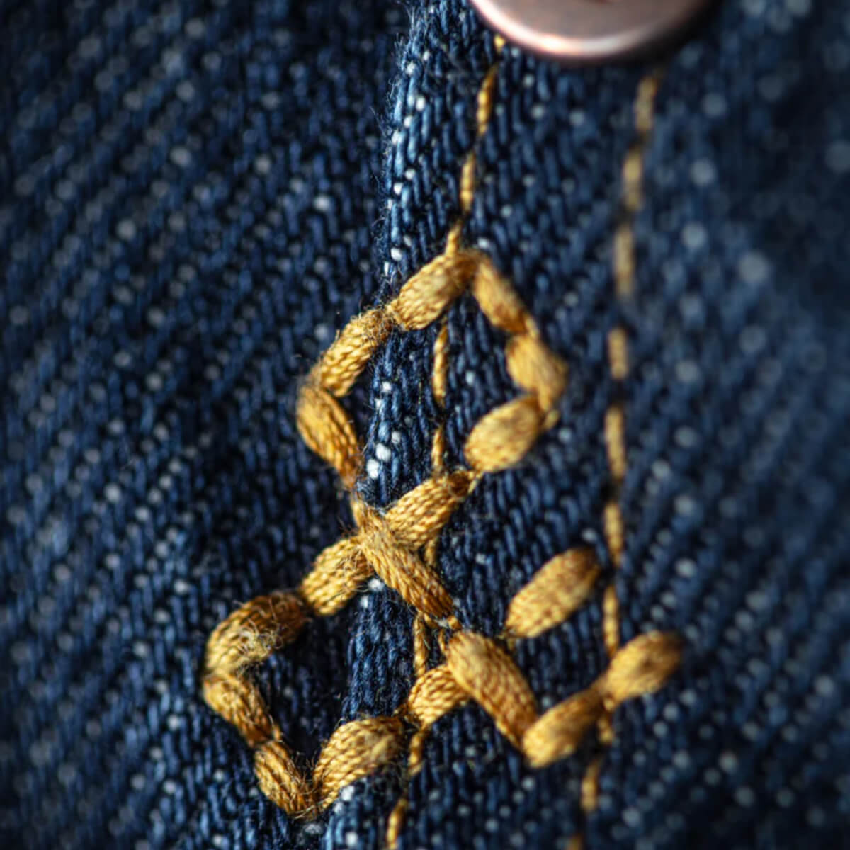 Close-up of gold embroidery on blue denim fabric.