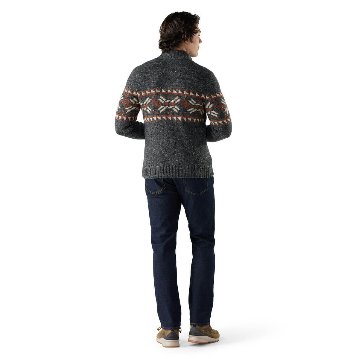 Person wearing a patterned sweater and dark jeans on a white background
