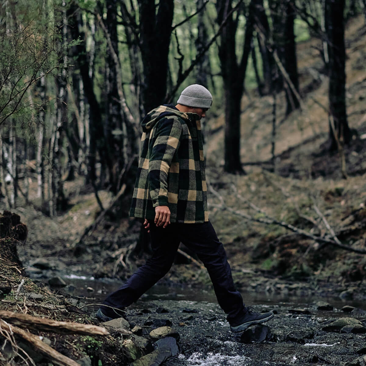 Person walking through a forest wearing a plaid jacket and beanie.