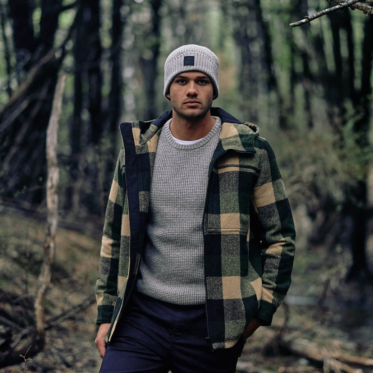 Man wearing a plaid jacket and beanie standing in a forest
