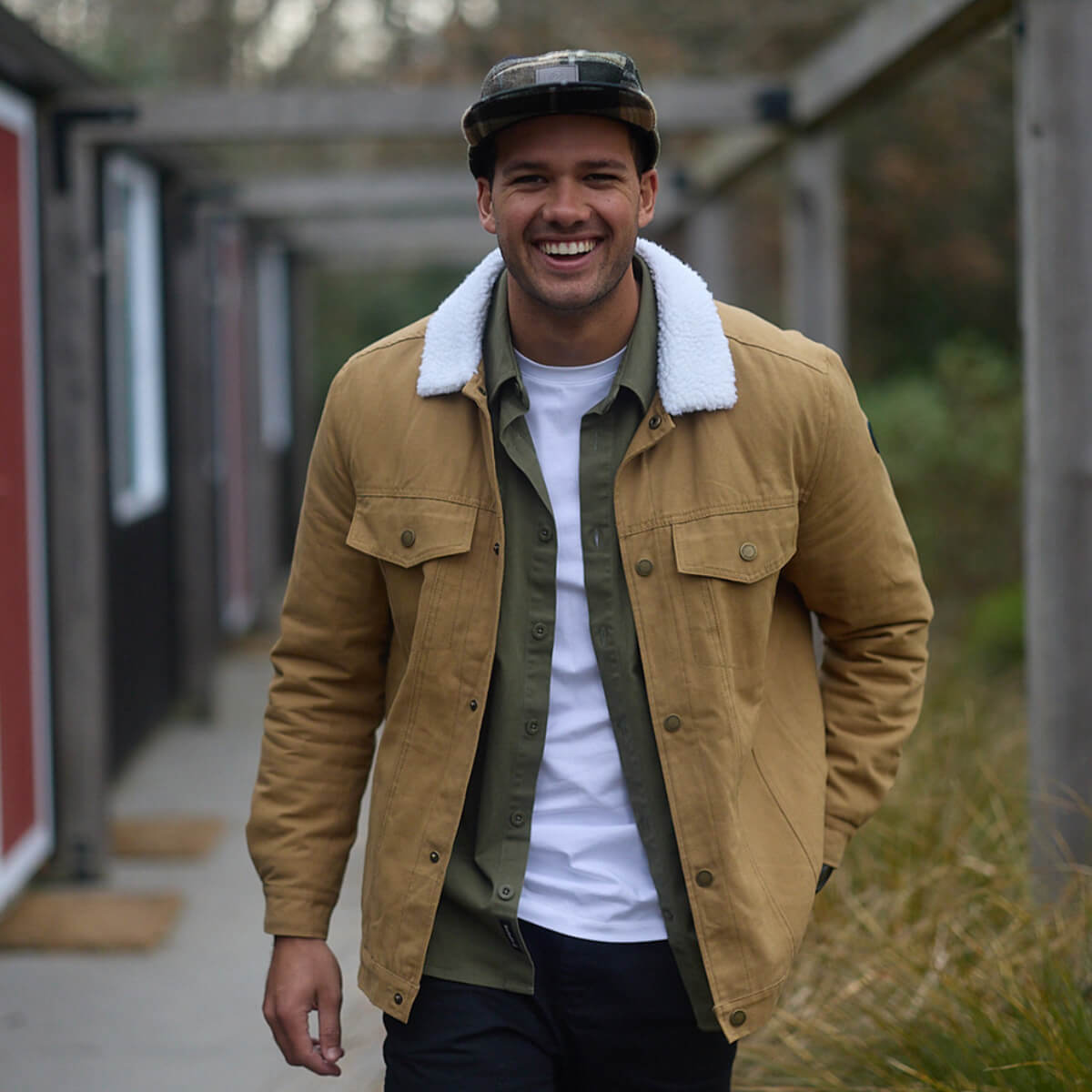 Man wearing a tan jacket with a white shirt and black pants, standing outdoors.