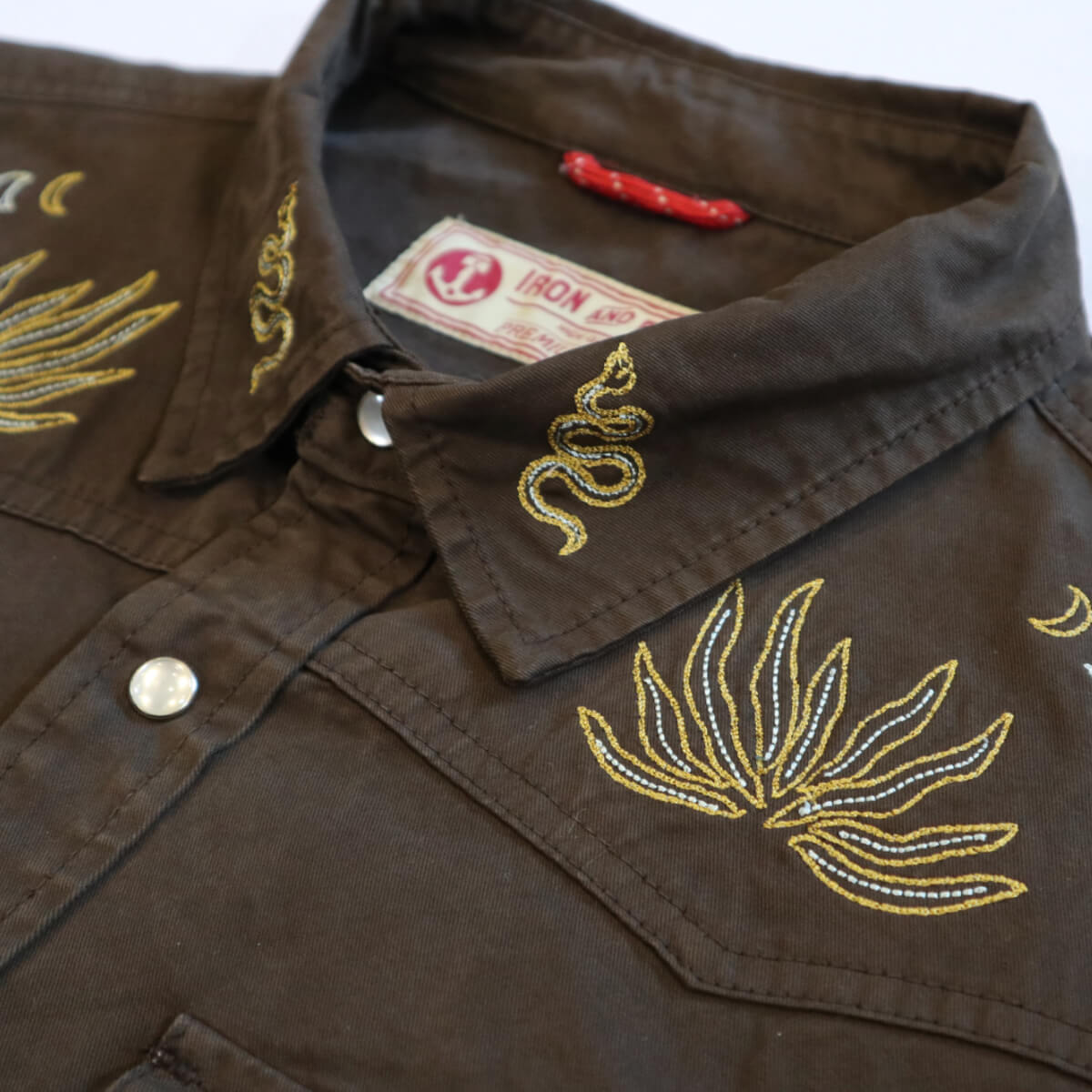 Brown shirt with gold embroidery and a visible brand label.