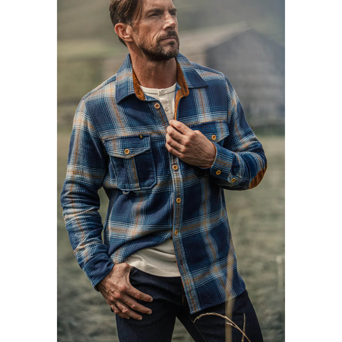 Man wearing a blue plaid shirt outdoors with a blurred background