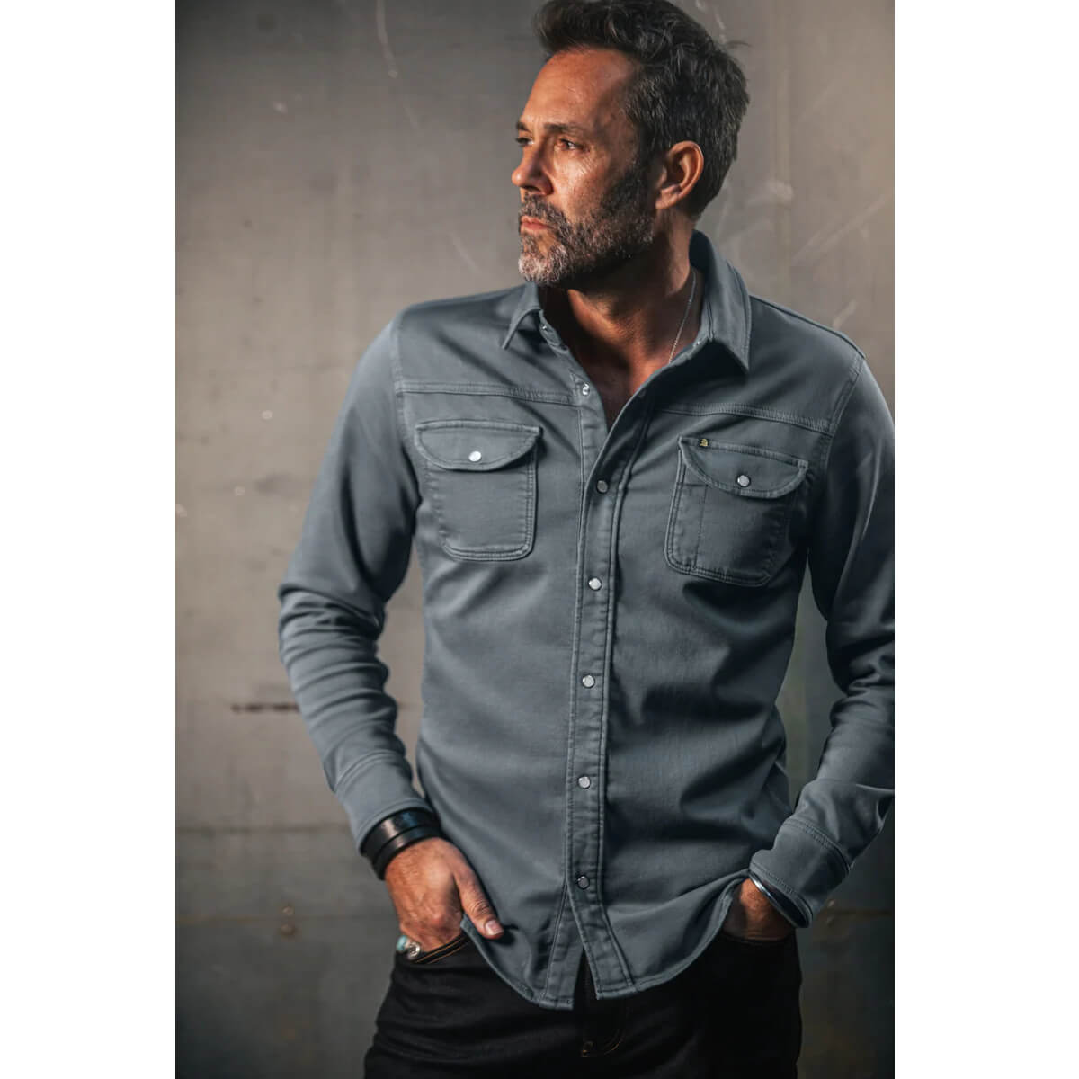 Man wearing a gray button-up shirt against a textured wall.